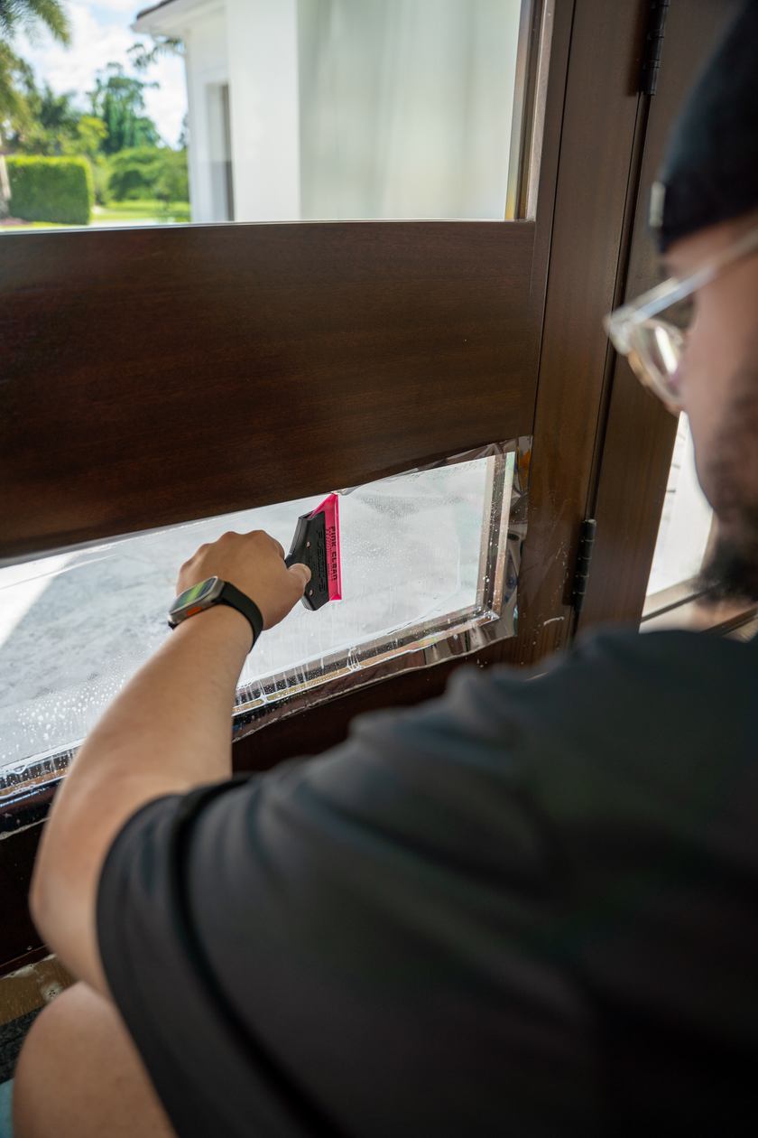 Installer making a squeegee pass across film on a door pane