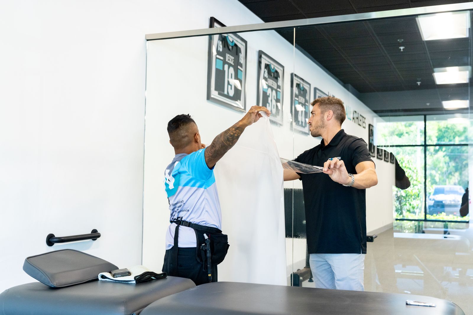 Two installers peeling the liner from a sheet of protective film at a glass wall