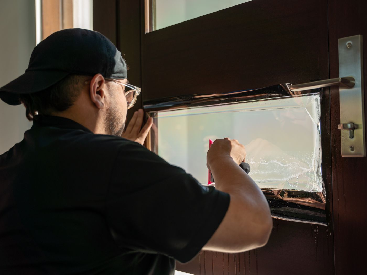 Installer working a sheet of protective film onto the glass panel of an entry door