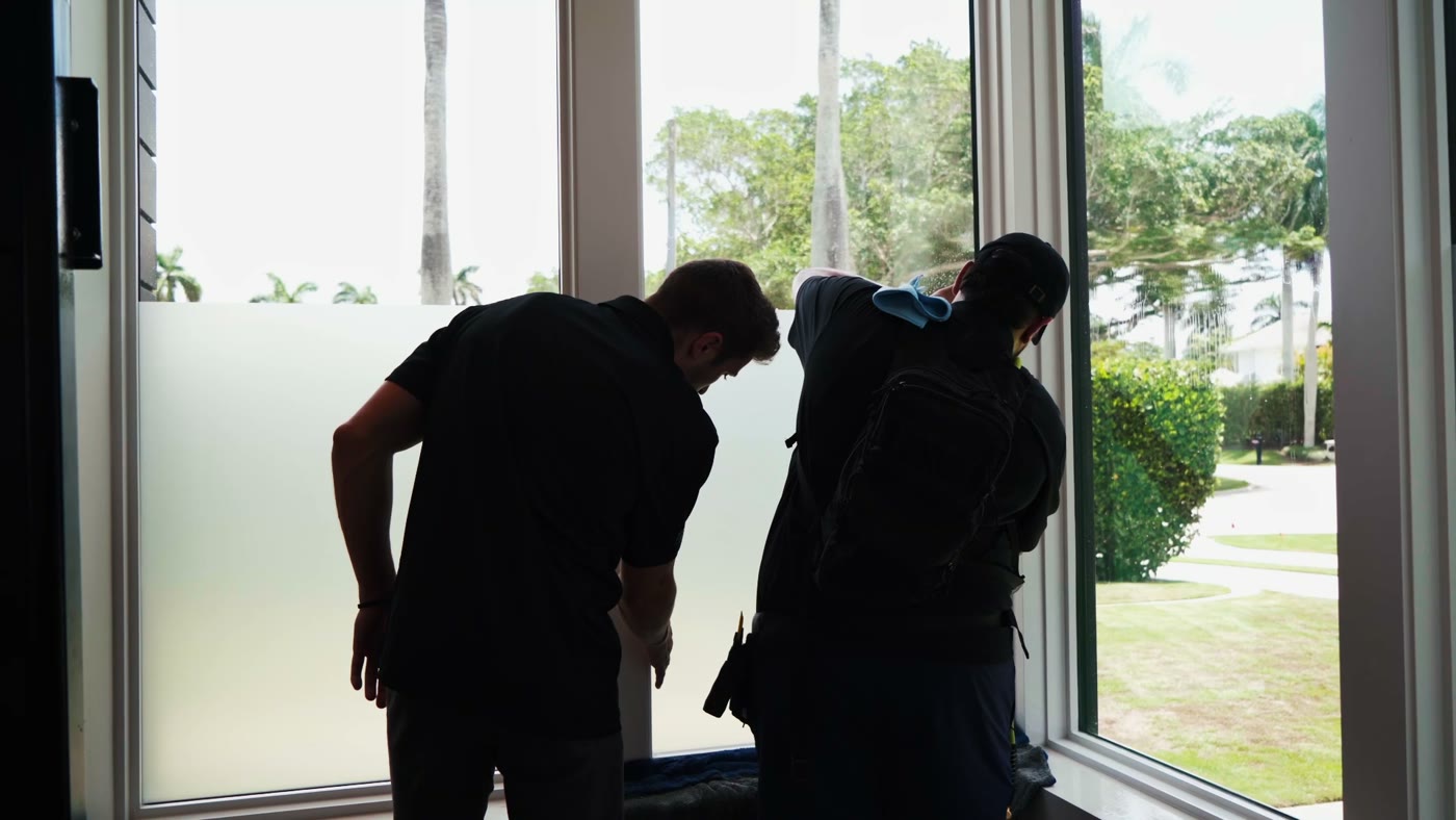 Two installers fitting privacy film to a full-height window